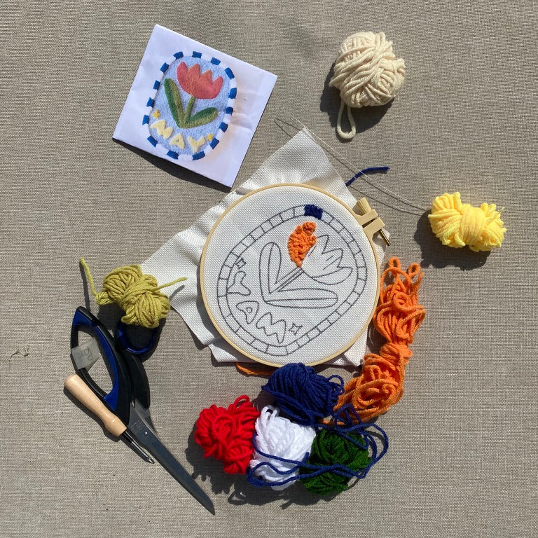 Embroidery hoop with floral design, scissors, yarn, and a small embroidered square on a beige surface.