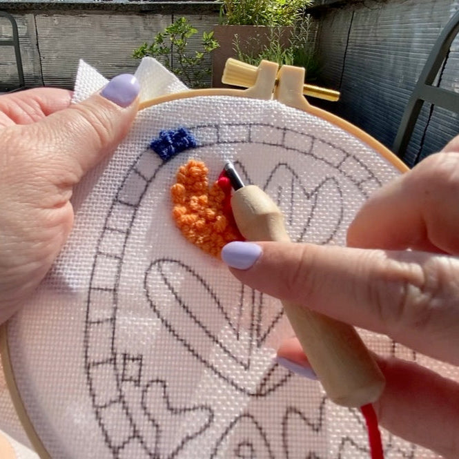 Person stitching a punch needle design on a hoop with a needle and thread.