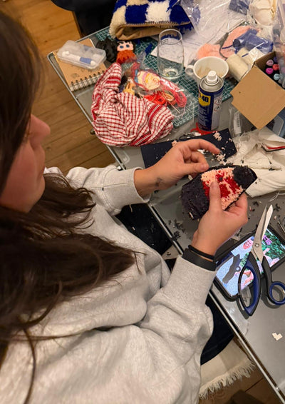 Person sitting at a table with various items including a phone, scissors, and a bottle.