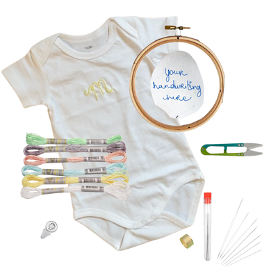 Baby onesie with embroidered design, embroidery hoop, threads, and tools on a white background