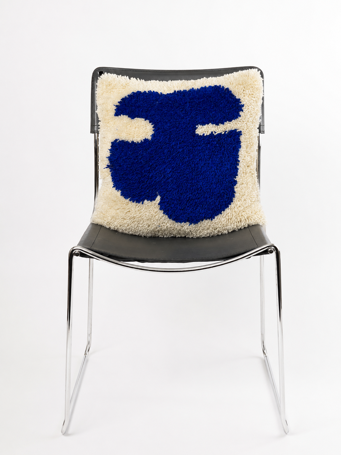 A modern black chair with a high back and chrome legs, featuring a plush cream and royal blue latch hook cushion.