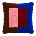 A square shaggy latch hook throw pillow with a geometric color-block pattern featuring brown, pink, red, and blue sections.