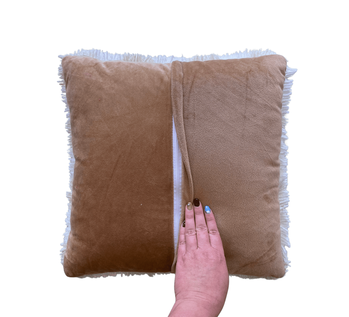 A square tan plush throw pillow with white fringe trim, shown against a solid green background with a hand holding the center seam to demonstrate its soft texture.