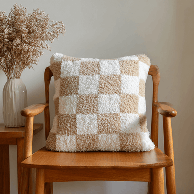 Checkered pillow on a wooden chair with a vase of dried flowers in the background
