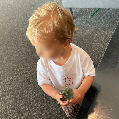 Child wearing a white shirt with a logo, sitting on a floor.