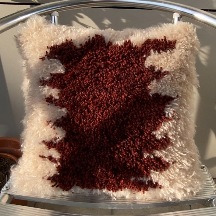 Decorative handmade latch hook pillow with a red leaf design on a metal chair