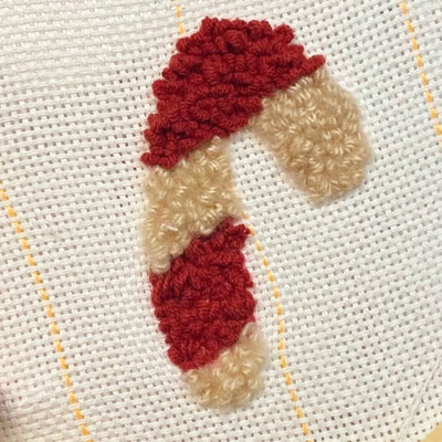 Embroidery hoop with a red and beige candy cane design held by a hand.