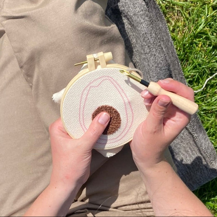 Person sitting on grass holding a embroidery hoop and punch needle